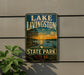 A vintage-style sign for Lake Livingston State Park in Texas, featuring a scenic landscape with a sunset over the lake and a bird in the foreground.
