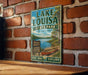 A vintage-style sign for Lake Louisa State Park in Florida, featuring a scenic illustration of a lake and surrounding nature.