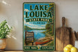A vintage-style sign for Lake Louisa State Park in Florida, featuring a scenic image of a lake, canoe, and surrounding nature.