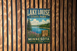 A vintage-style metal sign for Lake Louise State Park in Minnesota, featuring a scenic landscape with pine trees, a lake, and mountains.