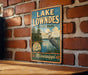 A vintage-style sign for Lake Lowndes State Park in Mississippi, featuring a scenic illustration of a bird and a lake.
