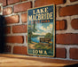 A vintage metal sign for Lake Macbride State Park in Iowa, featuring a scenic illustration of the park's landscape.