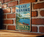 A vintage-style metal sign for Lake Manawa State Park in Iowa, featuring a scenic illustration of a lake, canoe, and surrounding landscape.