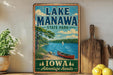 A vintage-style sign for Lake Manawa State Park in Iowa, featuring a scenic illustration of a lake, canoe, and surrounding landscape.