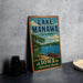 A vintage-style sign for Lake Manawa State Park in Iowa, featuring a scenic illustration of a lake, canoe, and surrounding landscape.