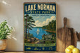 A vintage-style sign for Lake Norman State Park in North Carolina, featuring a scenic image of a lake surrounded by pine trees and a sailboat.