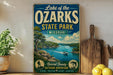A vintage-style sign for Lake of the Ozarks State Park, Missouri, featuring a scenic illustration of a lake surrounded by mountains and a boat on the water.