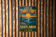A vintage metal sign for Lake of Three Fires State Park in Iowa, featuring a scenic landscape with a lake, forest, and sunset.