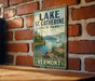 A vintage metal sign for Lake St. Catherine State Park in Vermont, featuring a scenic landscape with a sailboat on the lake.