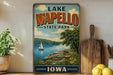 A vintage-style sign for Lake Wapollo State Park in Iowa, featuring a scenic landscape with a sailboat on the lake and lush greenery.