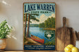 A vintage-style sign for Lake Warren State Park, featuring a scenic image of a lake, pine trees, and a canoe.