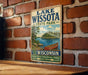 A vintage metal sign for Lake Wissota State Park in Wisconsin, featuring a scenic illustration of a lake with a canoe and surrounded by trees.