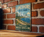 A vintage metal sign for Lakeshore State Park in Milwaukee, Wisconsin, featuring a scenic image of the park and its surroundings.