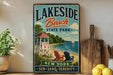 A vintage-style sign for Lakeside Beach State Park, featuring a lifeguard tower, beach chairs, and a sailboat on the water.