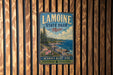 A vintage metal sign for Lamoine State Park in Maine, featuring a scenic landscape with pine trees, a rocky coastline, and a blue sky with clouds.