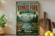 a vintage-style sign for the Land of the Yankees Fork State Park in Idaho, with a scenic mountain landscape and a river.