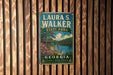 A vintage metal sign for Laura S. Walker State Park in Georgia, featuring a scenic landscape with a lake, bridge, and trees.