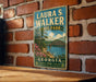 A vintage-style metal sign for Laura S. Walker State Park in Georgia, featuring a scenic landscape with a bridge and trees.