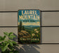A vintage metal sign for Laurel Mountain State Park in Pennsylvania, featuring a scenic mountain landscape with pine trees and flowers.