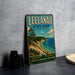 A vintage-style metal sign for Leelau State Park, Michigan, featuring a scenic landscape with a beach, mountains, and a lake.