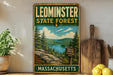 A vintage-style metal sign for Leominster State Forest in Massachusetts, featuring a scenic landscape with pine trees, a lake, and mountains.