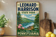 A vintage-style sign for Leonard Harrison State Park in Pennsylvania, featuring a scenic landscape with a lake, mountains, and trees.