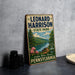 A vintage-style metal sign for Leonard Harrison State Park, featuring a scenic landscape with a lake, mountains, and trees.