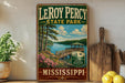 A vintage-style metal sign for LeRoy Percy State Park in Mississippi, featuring a scenic image of a wooden dock and a lake surrounded by trees.