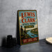 A vintage-style metal sign for Lewis and Clark State Park in Iowa, featuring illustrations of two men on a cliff overlooking a river and a scenic landscape.