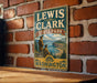 A vintage-style metal sign for Lewis and Clark State Park in Washington, featuring a scenic illustration of the park's landscape.