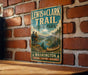A vintage metal sign for Lewis & Clark Trail State Park in Washington, featuring an illustration of a couple on a mountain with a canoe in the background.