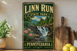 A vintage-style sign for Linn Run State Park in Pennsylvania, featuring a scenic image of a waterfall surrounded by pine trees and pink flowers.