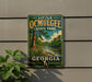 A vintage-style metal sign for Little Ocmulgee State Park in Georgia, featuring a scenic landscape with a river and trees.