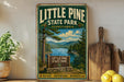 A vintage-style metal sign for Little Pine State Park in Pennsylvania, featuring a scenic landscape with pine trees, a lake, and mountains.