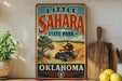 A vintage-style sign for Little Sahara State Park in Oklahoma, featuring an illustration of a person riding an ATV in a desert landscape.