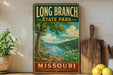 A vintage-style sign for Long Branch State Park in Missouri, featuring a scenic landscape with a lake, trees, and flowers.