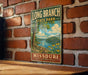 A vintage-style metal sign for Long Branch State Park in Missouri, featuring a scenic landscape with a lake, trees, and flowers.