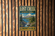 A vintage metal sign for Lost Creek State Park in Montana, featuring a scenic landscape with mountains, a river, and pine trees.