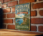A vintage-style sign for Louisiana Purchase State Park in Arkansas, featuring a scenic illustration of a river and a cliff overlooking the water.
