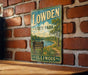 A vintage-style sign for Lowden State Park in Illinois, featuring a scenic landscape with a lake and trees, mounted on a brick wall.
