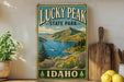 A vintage-style sign for Lucky Peak State Park in Idaho, featuring a scenic mountain landscape with a lake and a boat.