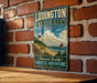 A vintage-style metal sign for Ludington State Park in Michigan, featuring a lighthouse and a beach scene, is displayed on a brick wall.