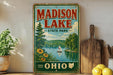 A vintage-style metal sign for Madison Lake State Park in Ohio, featuring a scenic illustration of a lake, trees, and a sailboat.