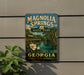 A vintage-style sign for Magnolia Springs State Park in Georgia, featuring a scenic landscape with a river, bridge, and flowers.