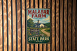 A vintage metal sign for Malabar Farm, featuring a farm scene with a barn and a dirt road, mounted on a wooden wall.