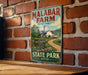 A vintage metal sign for Malabar Farm, featuring a farm scene with a barn and a dirt road, mounted on a brick wall.