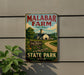 A vintage metal sign for Malabar Farm, featuring a farm scene with a barn, dirt road, and trees, mounted on a wall.