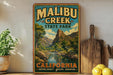 A vintage-style poster of Malibu Creek State Park in California, featuring a scenic mountain landscape with a river and lush vegetation.