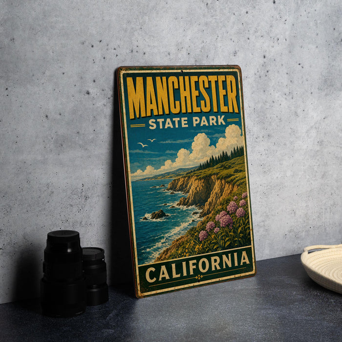 A vintage-style sign for Manchester State Park in California, featuring a scenic coastal landscape with cliffs, water, and flowers.
