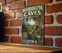 A vintage-style metal sign for the Maquoketa Caves State Park in Iowa, featuring a scenic image of the cave system and the park's name.